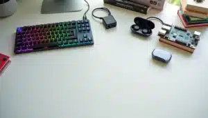 Sélection soignée de cadeaux tech disposés sur un bureau blanc en bois, illustrant un tech guide gift site avec clavier mécanique, écouteurs sans fil, hub USB-C et livres techniques de programmation
